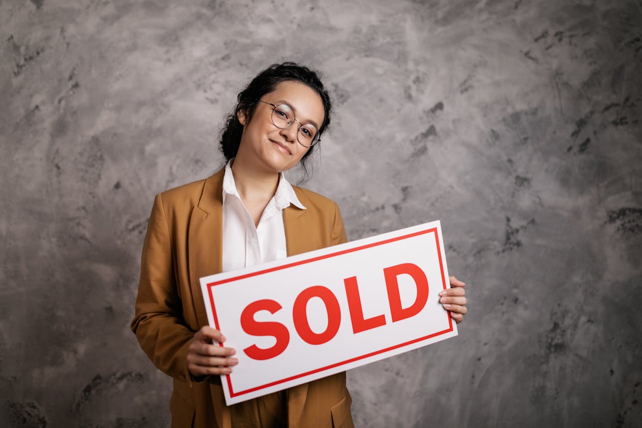 The Art of Drawing Readers In: Your attractive post title goes here Confident real estate agent holding a 'Sold' sign indoors, symbolizing successful property sale.